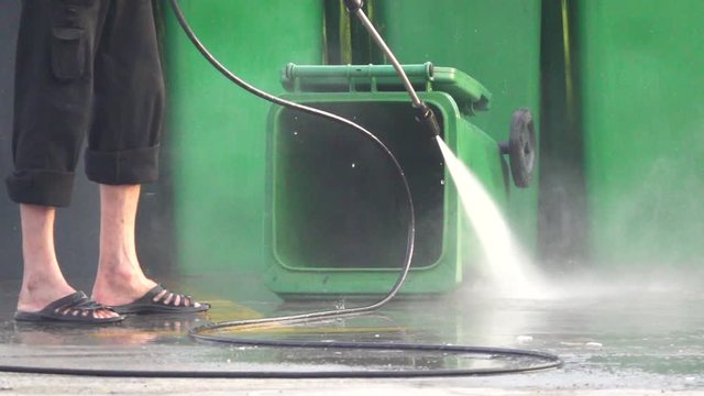 Cleaner cleans plastic dumpster with water from a hose under pressure, slow motion