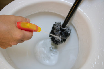 man makes the toilet cleaning in the house with toilet brush and spay foam