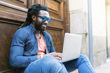 Portrait of african man sitting outside with laptop.