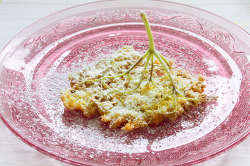 fried elderflower pancakes with powdered sugar on a pink glass dish