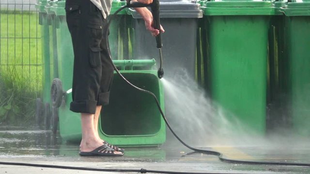 Cleaner cleans plastic dumpster with water from a hose under pressure, slow motion