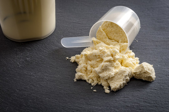 Fitness and sports concept with a spilled scoop of protein powder necessary nutrition for muscle recovery after an intensive workout, next to a protein shaker