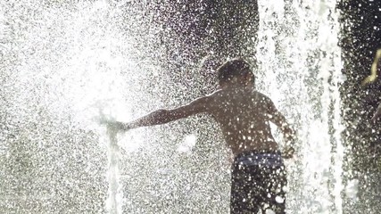Happy boy enjoys playing in the fountain, slow motion