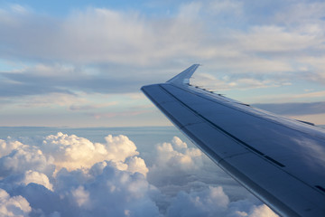 The wing of the plane on sky background during sunset. Air clouds illuminated by the rays of the...