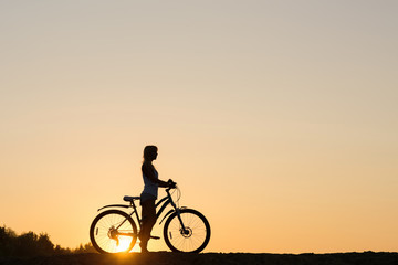 Fototapeta na wymiar Silhouette of a woman with her bicycle on the beach. You only live once!