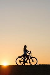 Fototapeta na wymiar Silhouette of woman with her bicycle on sunset background. My sunset exercise