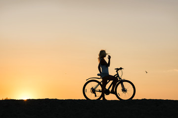 Fototapeta na wymiar Young woman with bicycle enjoying sunset. Taking in the beauty of it all...