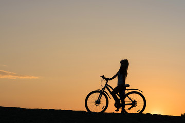Fototapeta na wymiar Silhouette of a woman with her bicycle on the beach. Lonely sunset cyclists