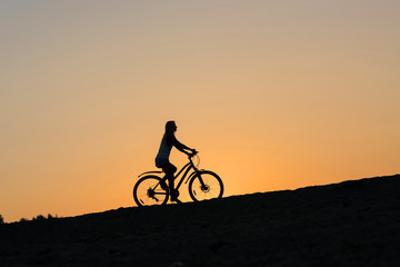 Obraz premium A silhouette of a female cyclist on the beach at sunset. Cycling off into the sunset