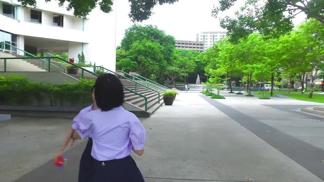Cute Asian Thai high schoolgirls student couple in school uniform are having fun playing chasing and catching a doll with her student friend with action camera moving