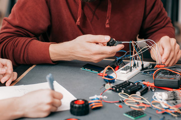 Electronics construction in laboratory. Unrecognizable engineer connecting components and cables to breadboard, educational experiment