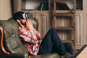 Excited man watching video in vr glasses. Young bearded male watching emotional movie in virtual reality headset, feeling shocked and thrilled. Cinema at home, innovation, entertainment concept