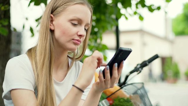 Pretty girl sitting outside and browsing internet on smartphone
