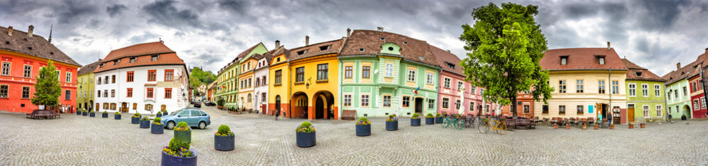 Panorama of the Sighisoara Citadel Square or Fortress Square. Colourful medieval houses with dramatic skies. Panoramic montage from 11 HDR images