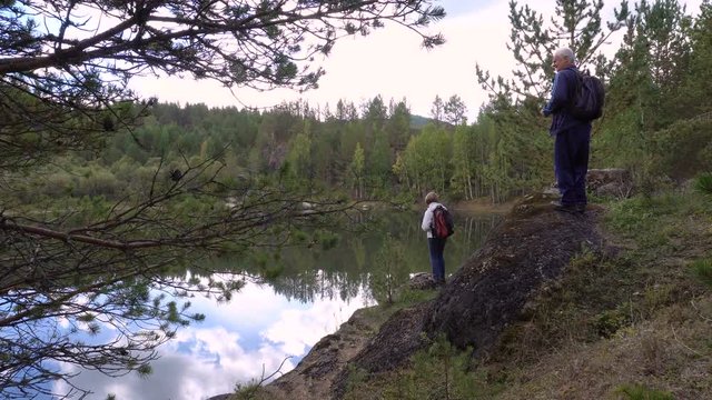 Woman and Man on the Shore of a Forest Lake Looking Photos on a Smartphone.