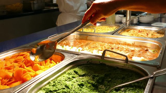 Buffet food indoor in restaurant with meat, potato, spinach, carrots, and other vegetables