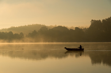 Człowiek wędkujący na łódce mglisty, złoty poranek. © rnfotografiapl