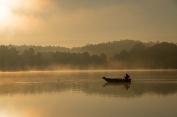 Człowiek wędkujący na łódce mglisty, złoty poranek. - obrazy, fototapety, plakaty