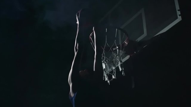 Slow motion shot of basketball player jumping and performing reverse dunk in the darkness