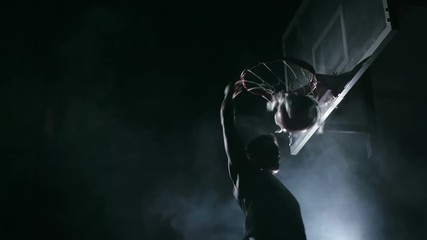 One handed slam dunk performed by basketball player in dark court with smoke in the background in slow motion - Powered by Adobe