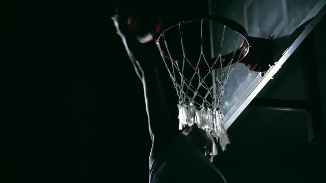 Basketball player performing one handed reverse dunk in dark court but ball missing the rim in slow motion