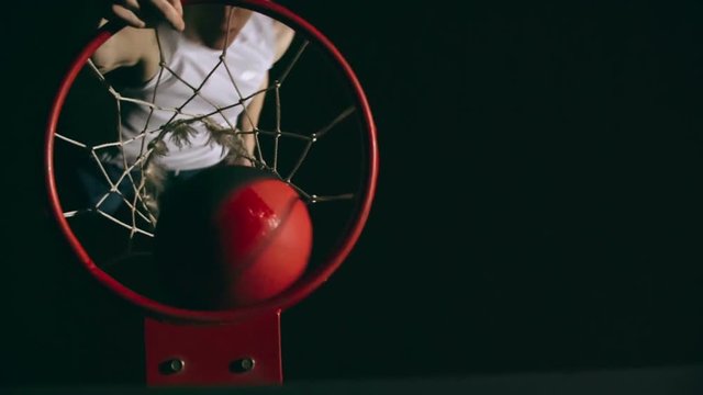 Top view of basketball player slamming ball into the net with one hand in slow motion in the dark court