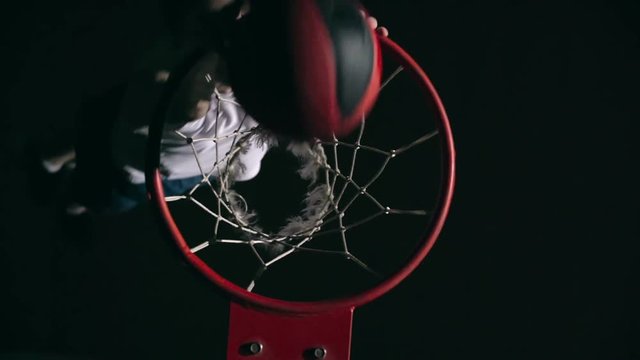 Top view of basketball player throwing ball into the net with both hands in slow motion in the darkness