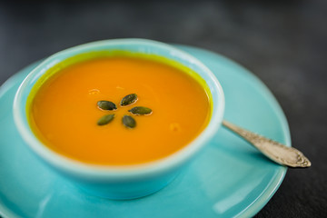 Tasty pumpkin soup in bowl on dark stone background with space for text.
