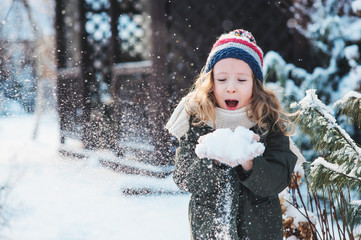 happy child girl playing with snow on snowy winter walk on backyard, making snowballs in the garden