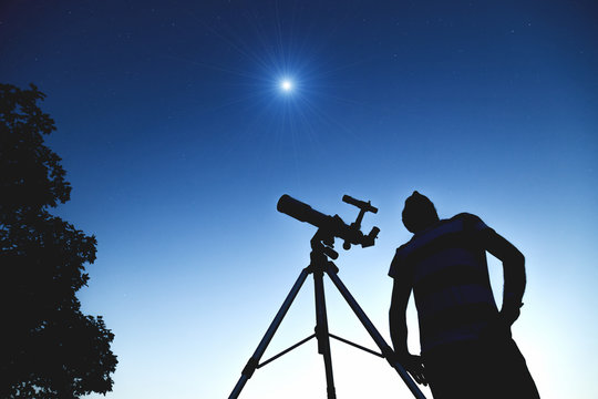 Man looking at the stars with telescope beside him.