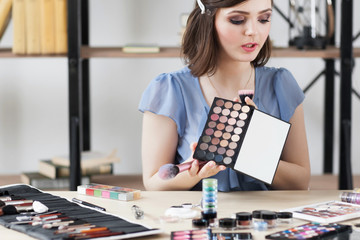 Fototapeta premium Cosmetics consult tells about eyeshadows palette. Young woman holding colorful eye cosmetics swatch. Makeup, beauty, fashion concept