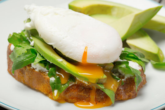Poached egg on piece of bread with avocado and arugula