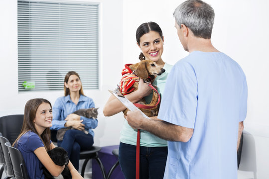 Woman Carrying Dachshund While Looking At Nurse In Clinic