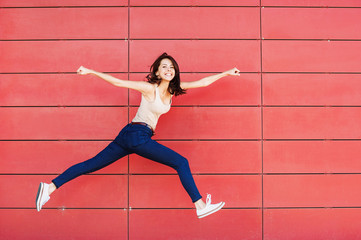 Joyful happy young woman jumping against red wall