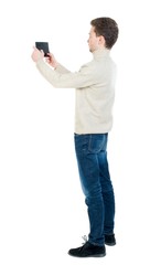 back view of standing business man photographing a phone or tablet. Curly short-haired man in a woolen white jacket standing sideways and holding the tablet horizontally.