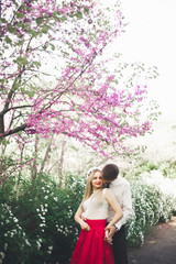Young beautiful couple kissing and hugging near trees with blossom in summer park