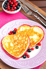 Homemade colored heart shaped pancakes with berries on porcelain