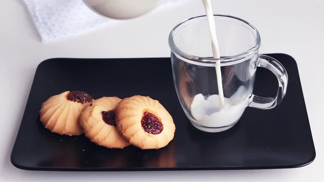 Serving breakfast - milk and cookies on black plate. Pouring fresh milk in transparent shockproof glass.
