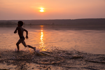 Boy running on river's beach against sunset