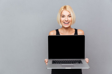 Happy cute young woman holding blank screen laptop