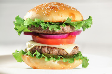 Big juicy traditional American burger with grilled meat and slices fresh vegetables closeup on a white plate on a wooden table. Food and beverages. Selective focus with shallow depth of field