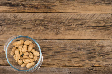 Peanuts in a glass bowl on the old wooden table.