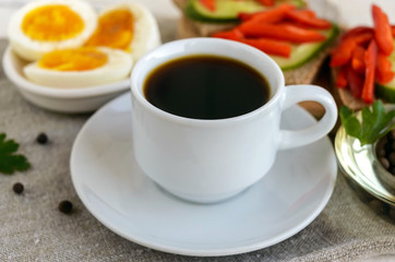 A cup of strong coffee (espresso), close-up and easy diet breakfast - boiled egg and brown bread with fresh vegetables (cucumber, paprika).