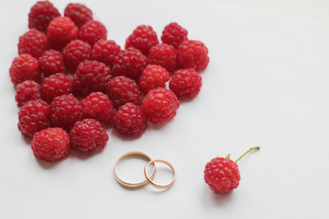the heart of raspberry and wedding rings on a white background