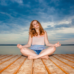 Girl on the wooden pier on the beach meditating on sunset. relaxation and peace concept