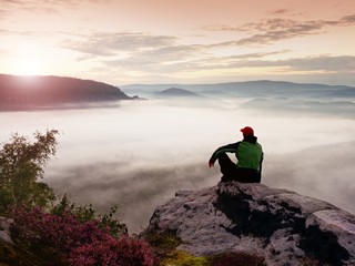 Man tourist sit on rock empire.Heather and branches above misty valley