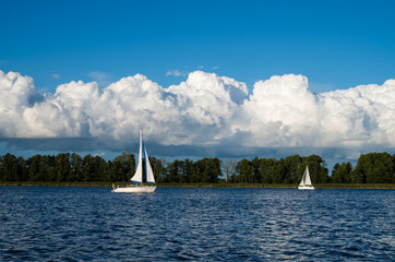 Dwa jachty żaglowe żeglujące po jeziorze, w tle rozbudowujące się chmury Cumulus