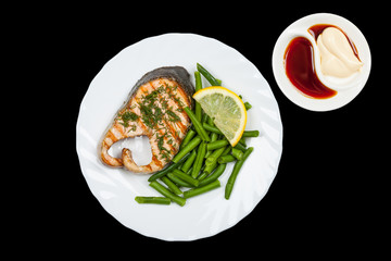 plate of grilled salmon steak and sauce isolated on black background