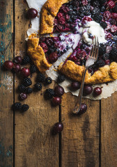Homemade garden berry galetta or crostata sweet pie with melted vanilla ice-cream scoop served with fresh berries on rustic wooden background. Top view, copy space, vertical composition
