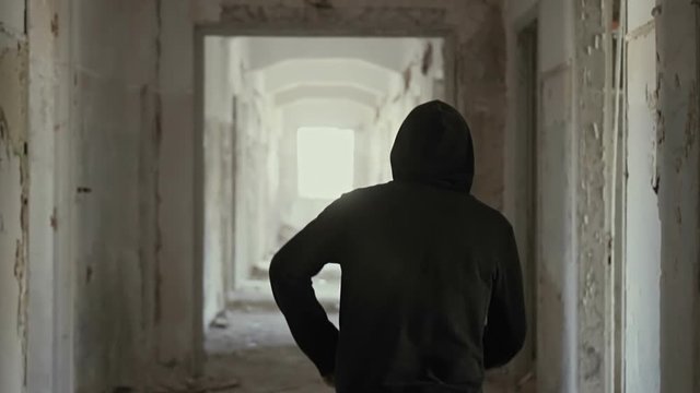 Hooded young man inside destroyed abandoned building,slow motion,dramatic